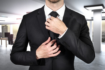 businessman ties his black tie in modern office