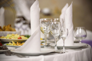 Glasses, forks, knives, napkins and decorative flower on a table served for dinner in cozy restaurant.