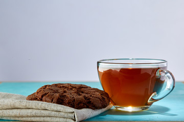 Glass cup of tea and chocolate cookies close-up on blue background.