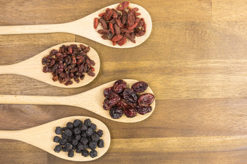 cranberries, aronia, berberis and goji berries on wooden spoons