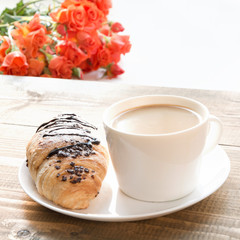 Freshly baked chocolate croissants and cup of coffee on wooden table. Breakfast concept.