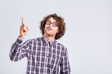 Curly nerd man in glasses with a stupid kind of funny emotion on a gray background.