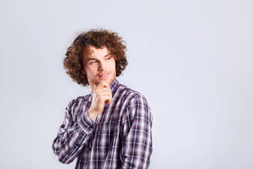 Fototapeta premium A curly-haired guy thinks with a serious emotion on a gray background.