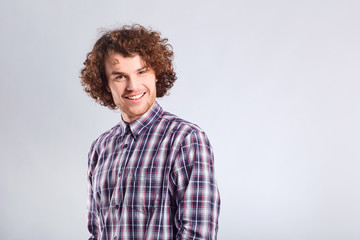 Fototapeta na wymiar Curly guy smiles with a positive emotion up against a gray background.