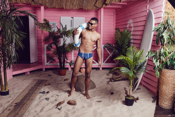 Sexy african american man in shorts standing on the sand and holding a life buoy.