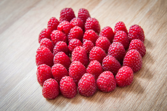 Raspberry berries heart symbol on wooden texture. Valentines day background.