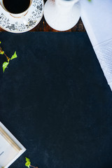 a Cup of coffee, books, a vase with green branches on a background of graphite Board, top view copyspace