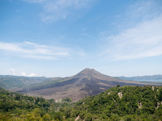 Fototapeta na wymiar Volcano, mountain covered forest, sky with clouds, traces of lava on the ground. Mount Batur Volcano in Kintamani. Mountain landscape, Bali. Travel concept.