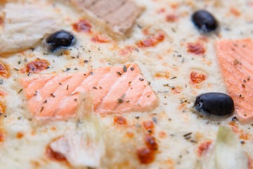 Pizza texture, food background. Close up of fresh baked mediterranean fish pizza with salmon, tuna and olives, macro