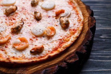 Hot seafood pizza with scallop, shrimps and mussels served on chopped wood, copy space. Italian food, restaurant or pizzeria menu concept