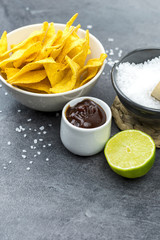 Tortilla chips with barbecue dip on a black stone table.