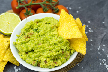 Avocado dip guacamole with tortilla chips in a white bowl on a black stone table. Traditional Mexican appetizer.