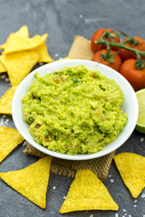 Avocado dip guacamole with tortilla chips in a white bowl on a black stone table. Traditional Mexican appetizer.
