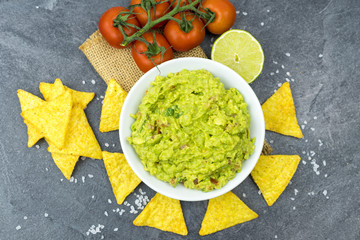 Avocado dip guacamole with tortilla chips in a white bowl on a black stone table. Traditional Mexican appetizer.