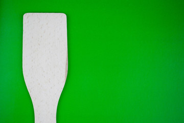 A wooden kitchen spatula on a green background.