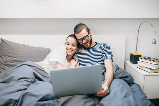 Young Couple Watching A Movie On Their Laptop In Bed 