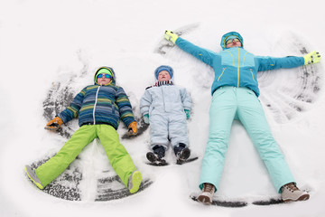 A young lady in a blue ski suit plays football with children in the snow. Yellow sled, sunglasses, bright clothes. Girl happy outdoors. Fun winter vacation for the whole family. Green soccer ball