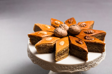 Traditional pakhlava baklava pastry from Azerbaijan made of walnuts and almonds with honey in round white plate cake stand on grey background, Novruz eastern new year spring celebration concept 