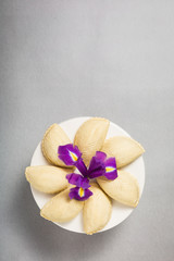 Fototapeta na wymiar Novruz traditional pastry shekerbura in round white plate cake stand with bouquet purple lilac flowers fleur de lis on grey background, spring celebration in Azerbaijan, greeting card copy space