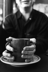 Cropped view at a young man holding coffe cup both hands in a coffe shop