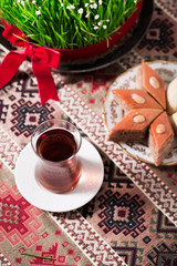 Novruz setting table decoration, tea in  tulip shape glass on ethnic motives rustic table cloth with wheat grass, dyed eggs, traditional sweets, samovar, new year sring celebration, nature awakening