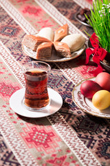 Novruz setting table decoration, tea in  tulip shape glass on ethnic motives rustic table cloth with wheat grass, dyed eggs, traditional sweets, samovar, new year sring celebration, nature awakening