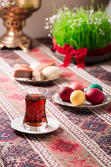 Novruz setting table decoration, tea in  tulip shape glass on ethnic motives rustic table cloth with wheat grass, dyed eggs, traditional sweets, samovar, new year sring celebration, nature awakening