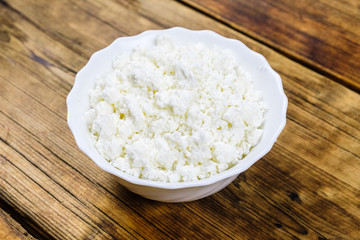 Close-up homemade fresh cottage cheese on white plate on wooden background.