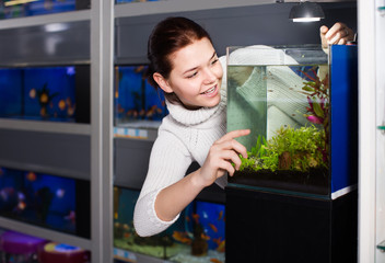 Fototapeta na wymiar Girl with interest looking at small fry fish in aquarium with seaweed in aquarium shop