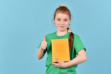 Obraz premium Schoolgirl with a book. A girl on a blue background. Isolated children.