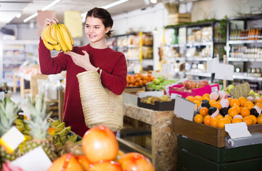 Obraz premium Portrait of brunette girl buying ripe bananas in supermarket