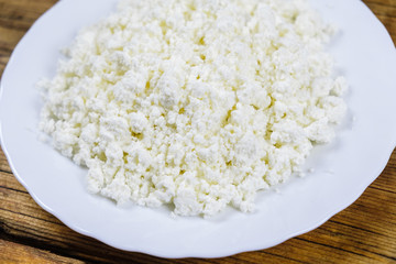 Close-up homemade fresh cottage cheese on white plate on wooden background. Side view.