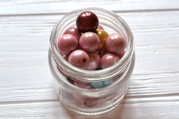 Colorful pearl beads in a glass jar on the white wodden background.