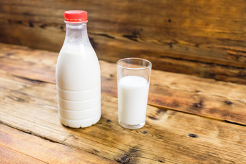 Bottle of fresh farm milk with red lid and glass of milk on wooden background In the center of photo
