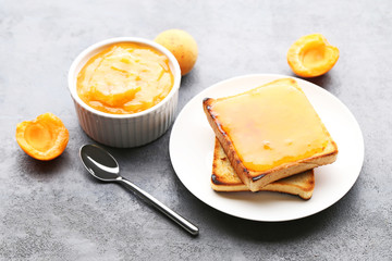 Apricot jam in bowl with bread toasts on grey wooden table
