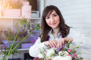 Florist workplace. Young woman arranging a beautiful bouquet with white roses, eustomas, leaves, ranunculus flowers and gypsophila in flower shop.