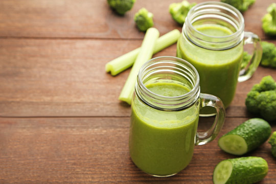 Bottles of juice with broccoli, celery and cucumber on brown wooden table