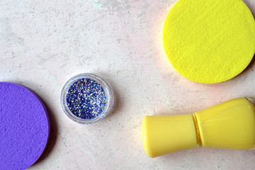 Creative beauty background. Yellow nail polish, sequins and purple sponges. Bright trendy colors.