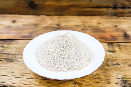 Close-up heap with wheat flour coarse in white plate on wooden background.