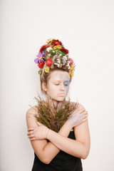 A young woman with flowers on her head and hands. Spring image with flowers. Man with a colorful plant. The girl and the blooming haircuts and brocade on her face.