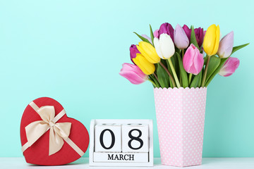 Bouquet of tulips with gift box and calendar cubes on wooden table
