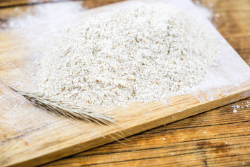 Close-up heap with rye flour coarse and grain on a wooden board. Side view.