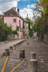 Fototapeta na wymiar Cobblestone road moving up the hill of Montmartre passing pink house and other old buildings in autumn Paris, France