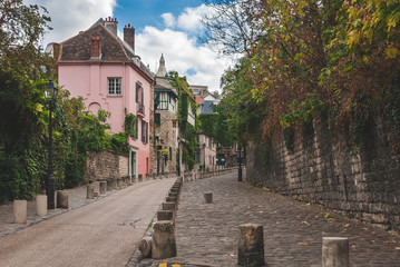 Beautiful old houses standing along cobblestone pavement and wall up the hill of Montmartre in Paris, France