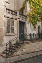 Beautiful old house with weathered stairs, door and window shutters and greenery covering wall on Montmartre, Paris