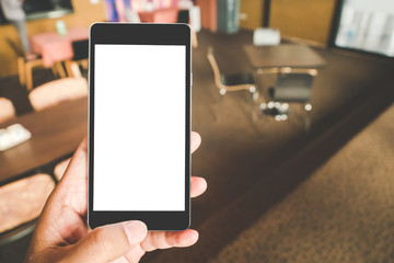 Hand holding black mobile smart phone with blank black screen in coffee shop cafe. technology and lifestyle concept.