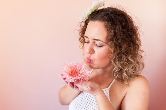 Beautiful curly woman holding pink flower on color background at home. Hello Spring concept.