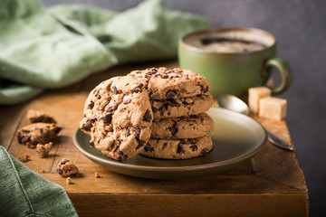 Chocolate chip cookies on green plate with cup of coffee on old wooden table. Selective focus.