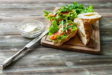 Croissants with smoked salmon, cottage cheese, fresh salad and herbs on a wooden background.