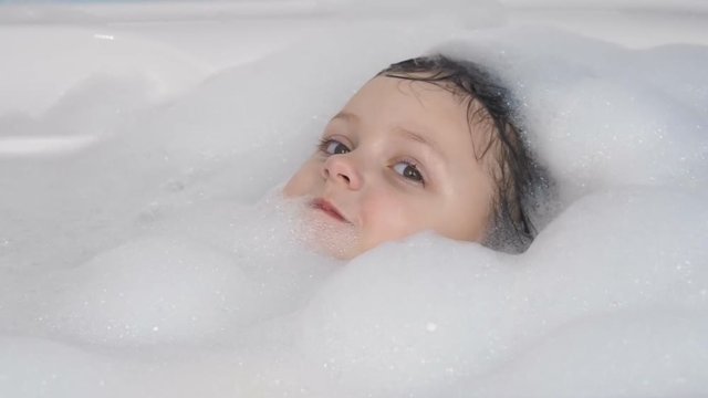 The child takes a bath. Happy little girl in foam in the bathroom.